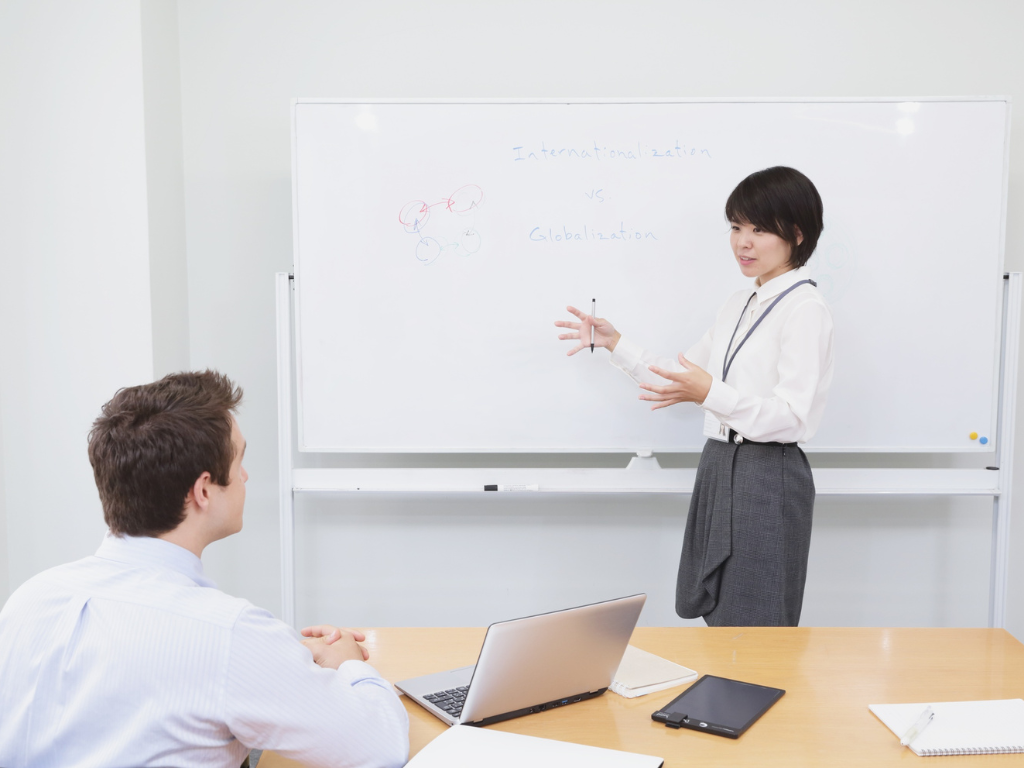 Teacher pointing at a whiteboard while explaining globalization to students in a classroom.